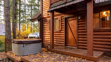 A log cabin with a wooden deck, a hot tub, and a stone wall.