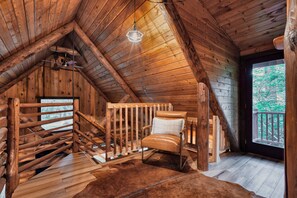 Un intérieur en bois avec un plafond en pente, une chaise en bois, un luminaire suspendu et une vue par une fenêtre.