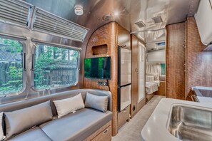 Un intérieur de camping-car compact comprenant un canapé, un téléviseur à écran plat, un réfrigérateur et une petite kitchenette.