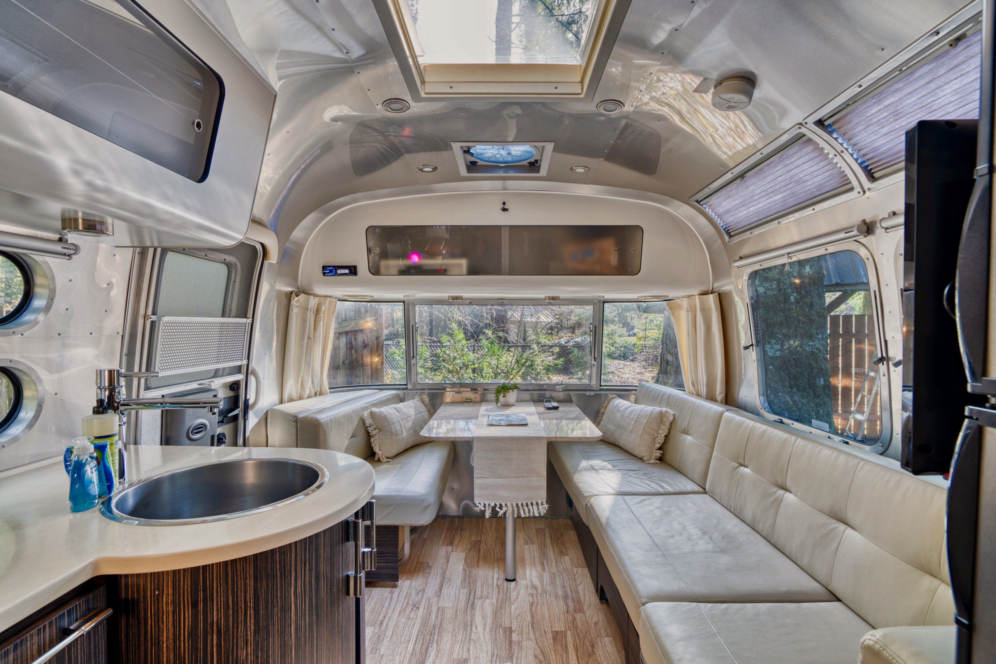 A compact RV interior with a kitchenette, a dining area, and a seating space with a view.