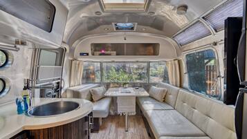 A compact RV interior with a kitchenette, a dining area, and a seating space with a view.