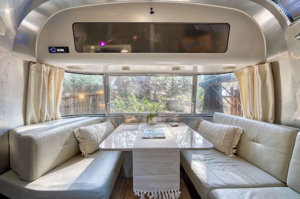Ein gemütliches Wohnmobil-Interieur mit einer Sofagarnitur, einem Tisch und einem Fenster mit Vorhängen.