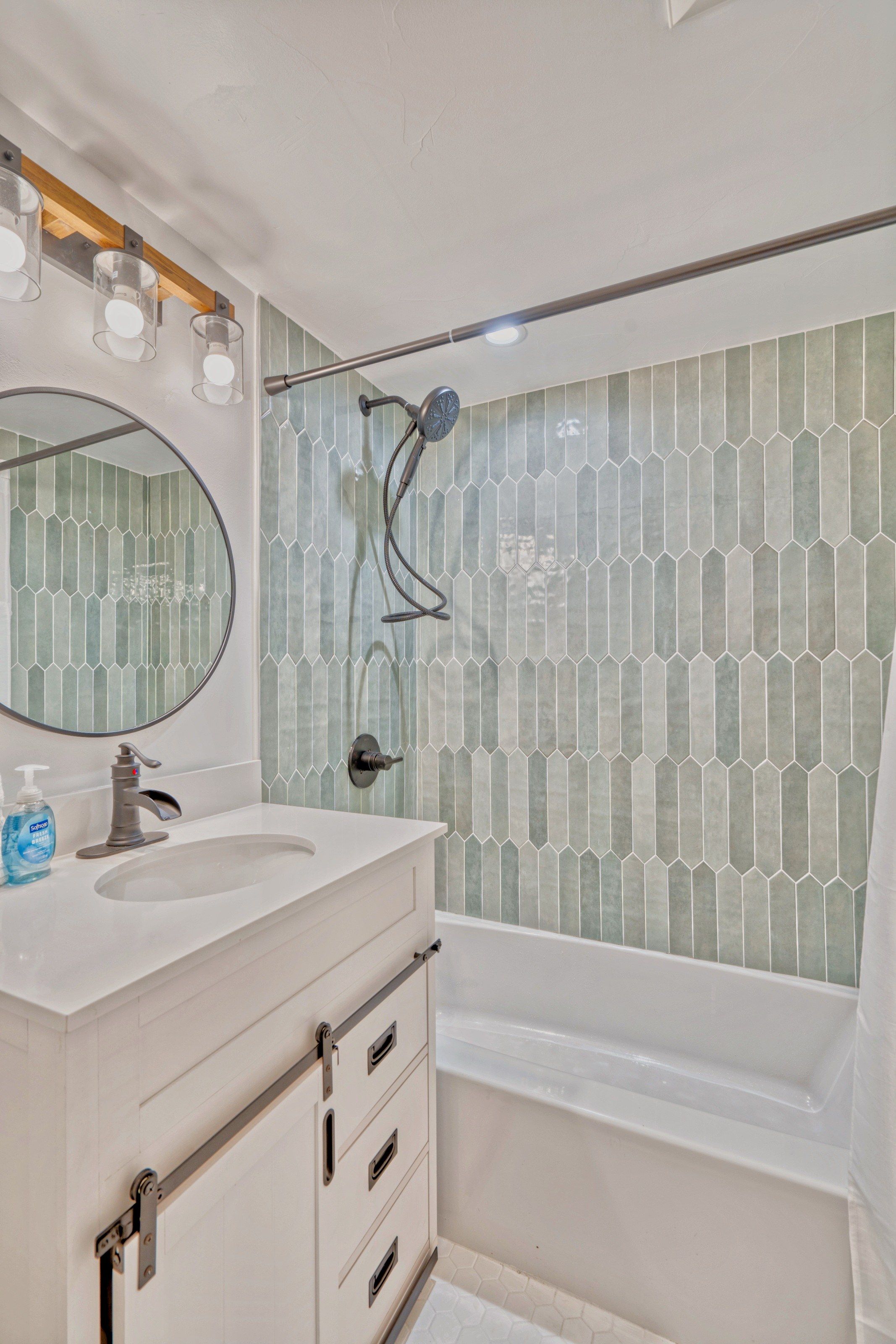 Une salle de bain avec un meuble-lavabo blanc, un miroir, une douche avec une porte en verre et des carreaux à motifs hexagonaux.