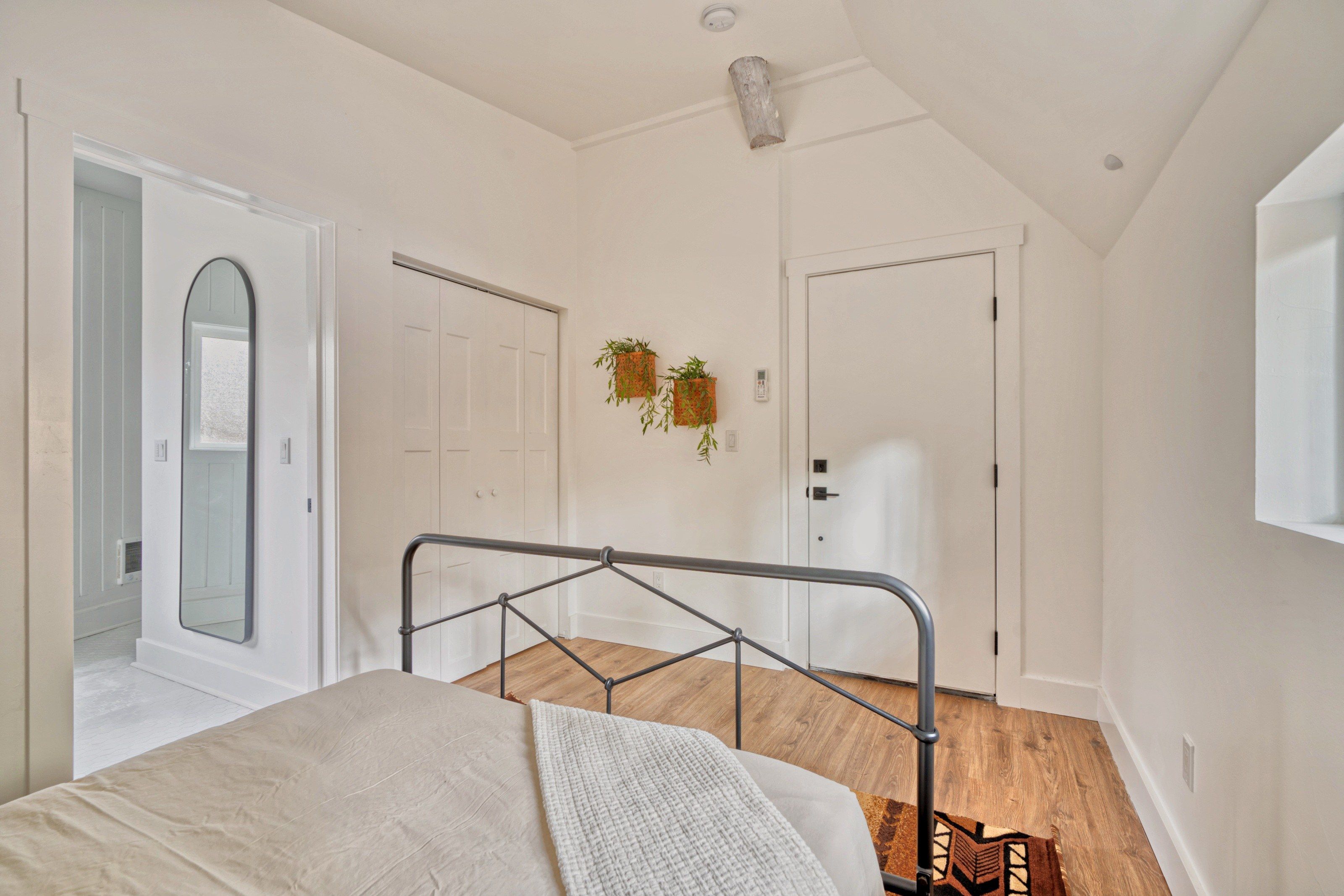Une chambre à coucher avec un lit, une porte blanche, une fenêtre et une plante accrochée au mur.