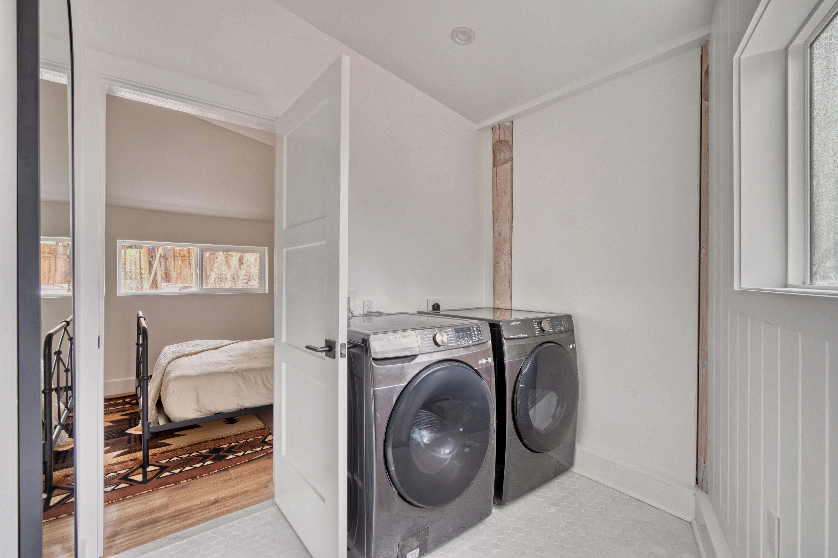 A laundry room with two front-loading washing machines, a bed with a patterned rug, and a staircase leading to an upper level.
