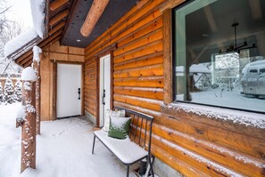A wooden cabin with a bench and a door, surrounded by snow.