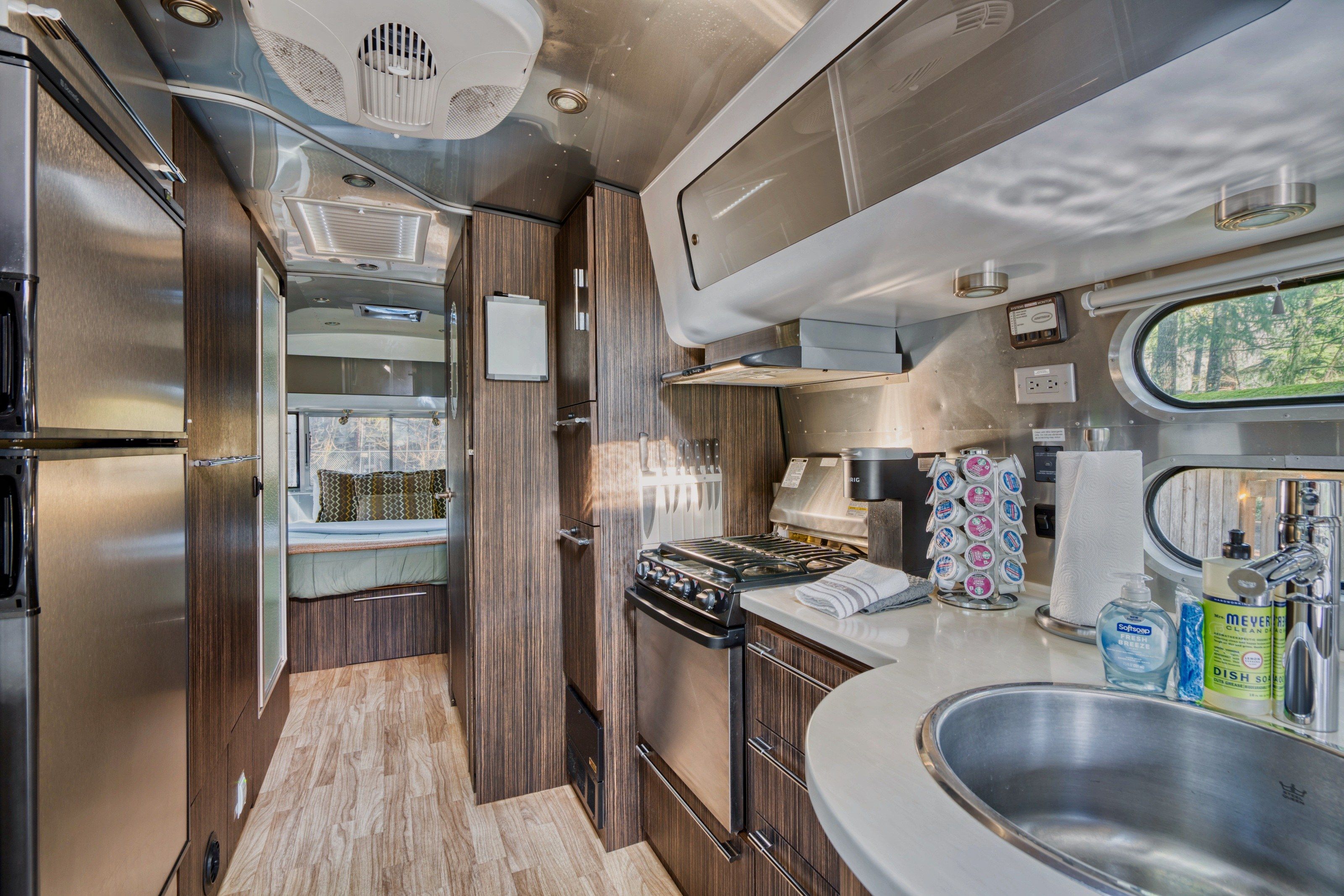 Een kleine keuken in een camper, met een kookplaat, wasbak en een klein raam.