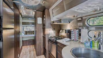 Een kleine keuken in een camper, met een kookplaat, wasbak en een klein raam.