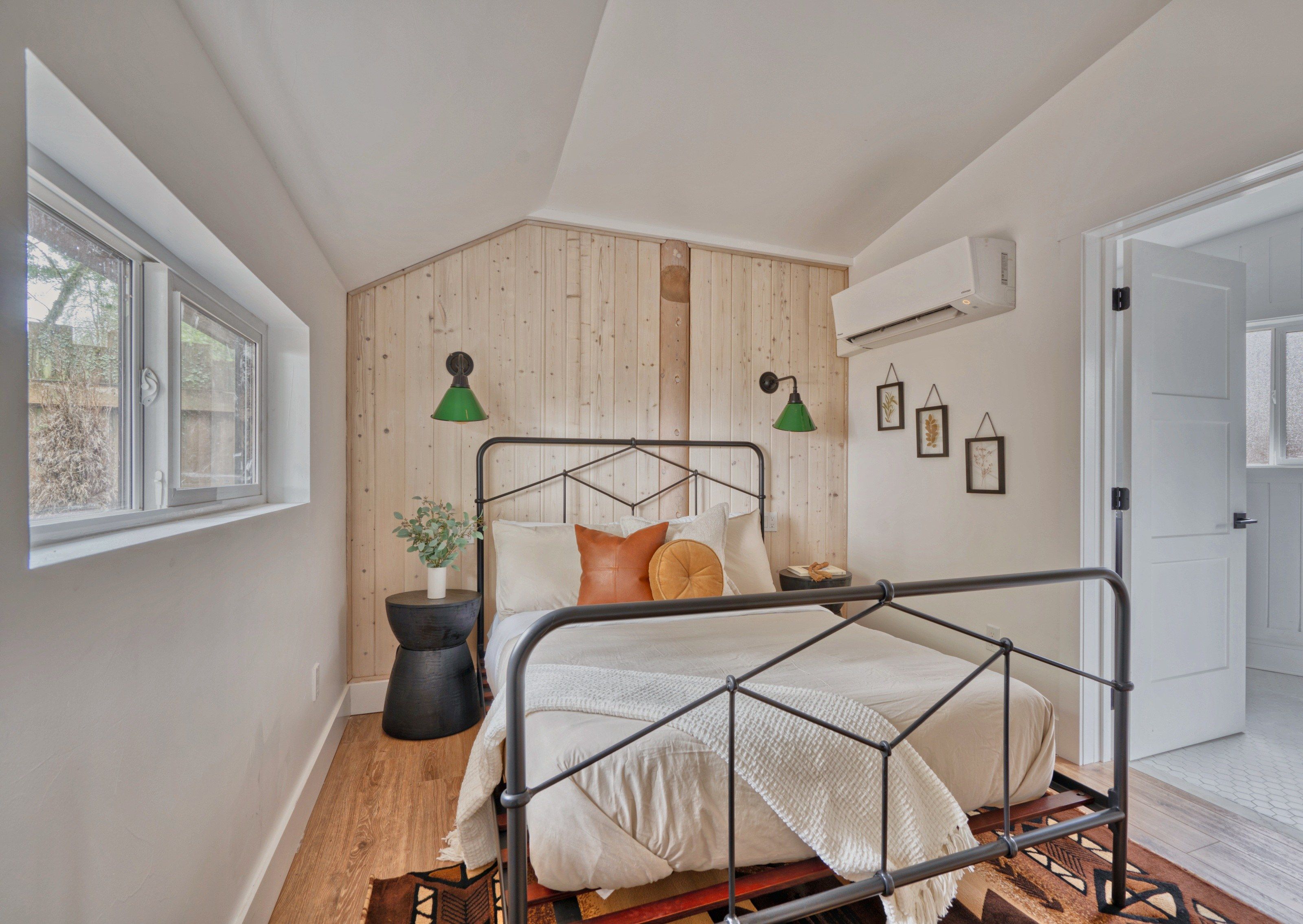 A bedroom with a metal bed frame, a window, a potted plant, and a wall-mounted air conditioner.