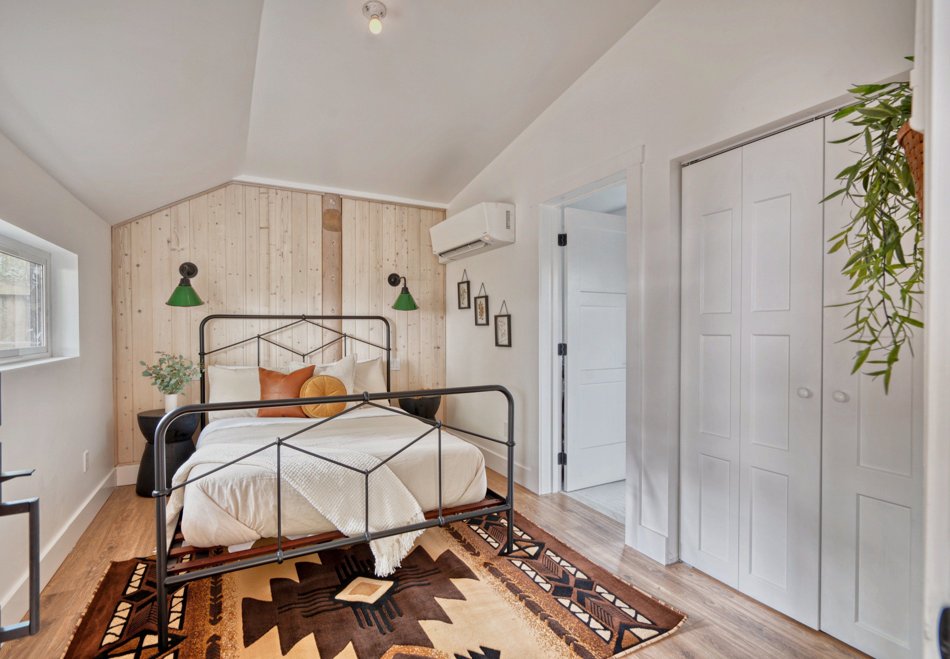 A modern bedroom with a metal bed frame, a wooden wall panel, a white door, and a hanging plant.