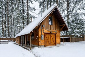 A wooden cabin with a steeply pitched roof, a front door, and a chimney.