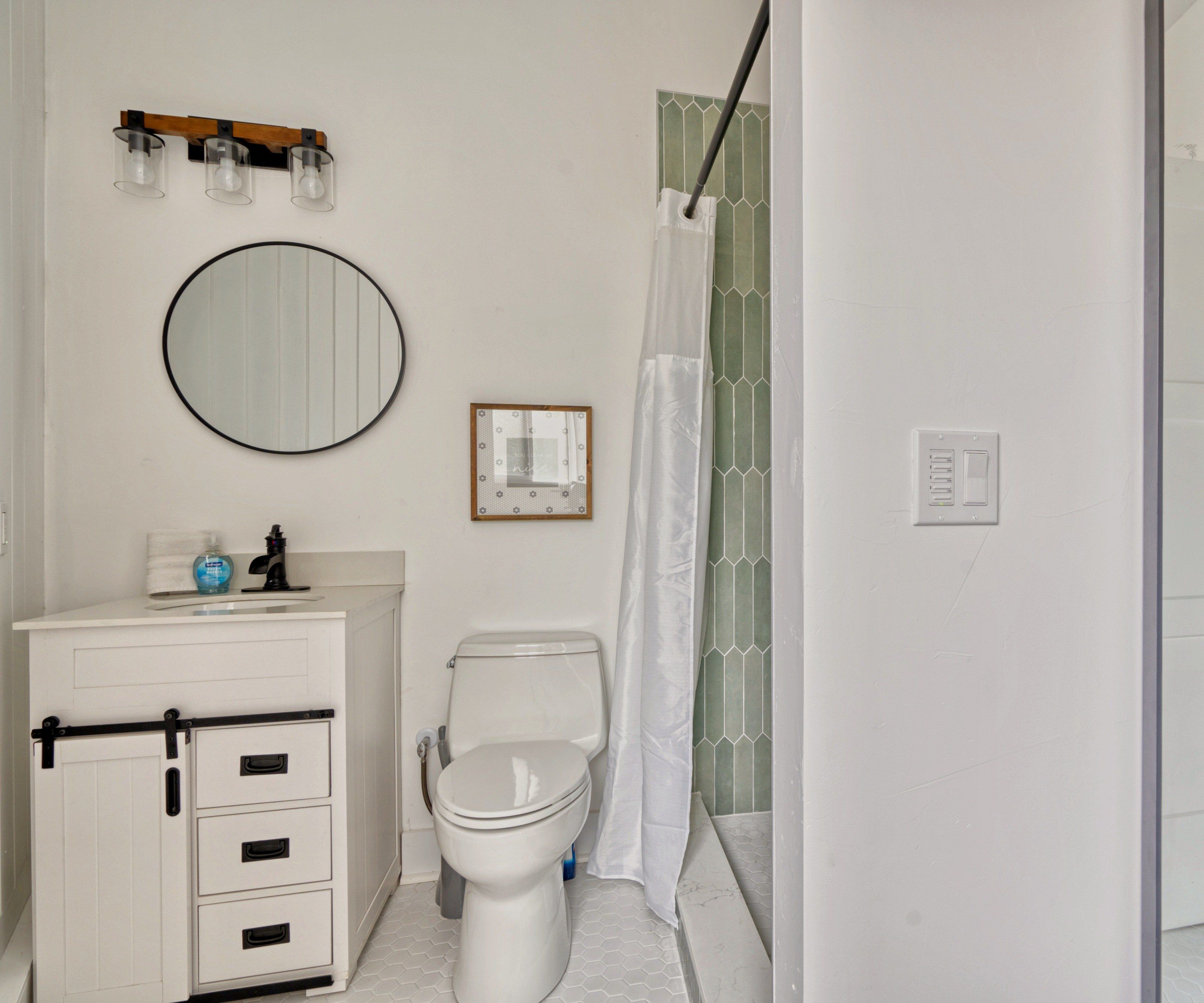 A bathroom with a toilet, a sink with a mirror, a shower curtain, and a small framed picture on the wall.