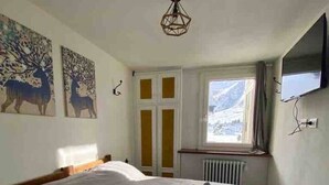 Ein Schlafzimmer mit einem großen Bett, zwei Hirschgemälden, einem Fenster mit Bergblick und einem Fernseher an der Wand.