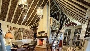 A cozy living room with a fireplace, a sofa, a dining area, and a staircase leading to an upper level.
