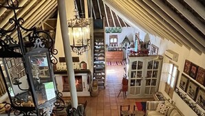 A spacious loft with high ceilings, exposed beams, and a central staircase. The room features a cozy seating area with a sofa and armchairs, a dining table, and a fireplace.