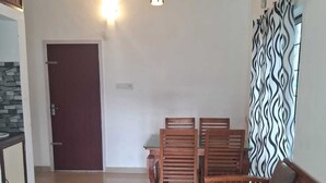 Ein großzügiger Wohnbereich mit einer Sofagarnitur, Holzstühlen und einem Esstisch. Ein Deckenventilator und eine Pendelleuchte sind sichtbar.