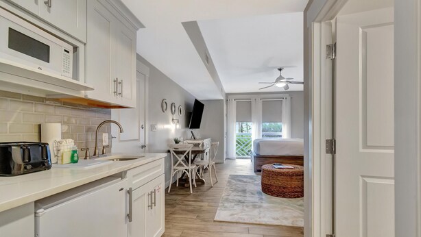 A modern kitchen with white cabinets, a microwave, and a toaster. There is a dining area with a table and chairs, and a wicker basket on the floor.