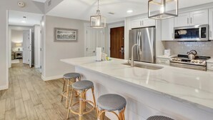 A modern kitchen with white cabinetry, stainless steel appliances, and a large island with bar stools.