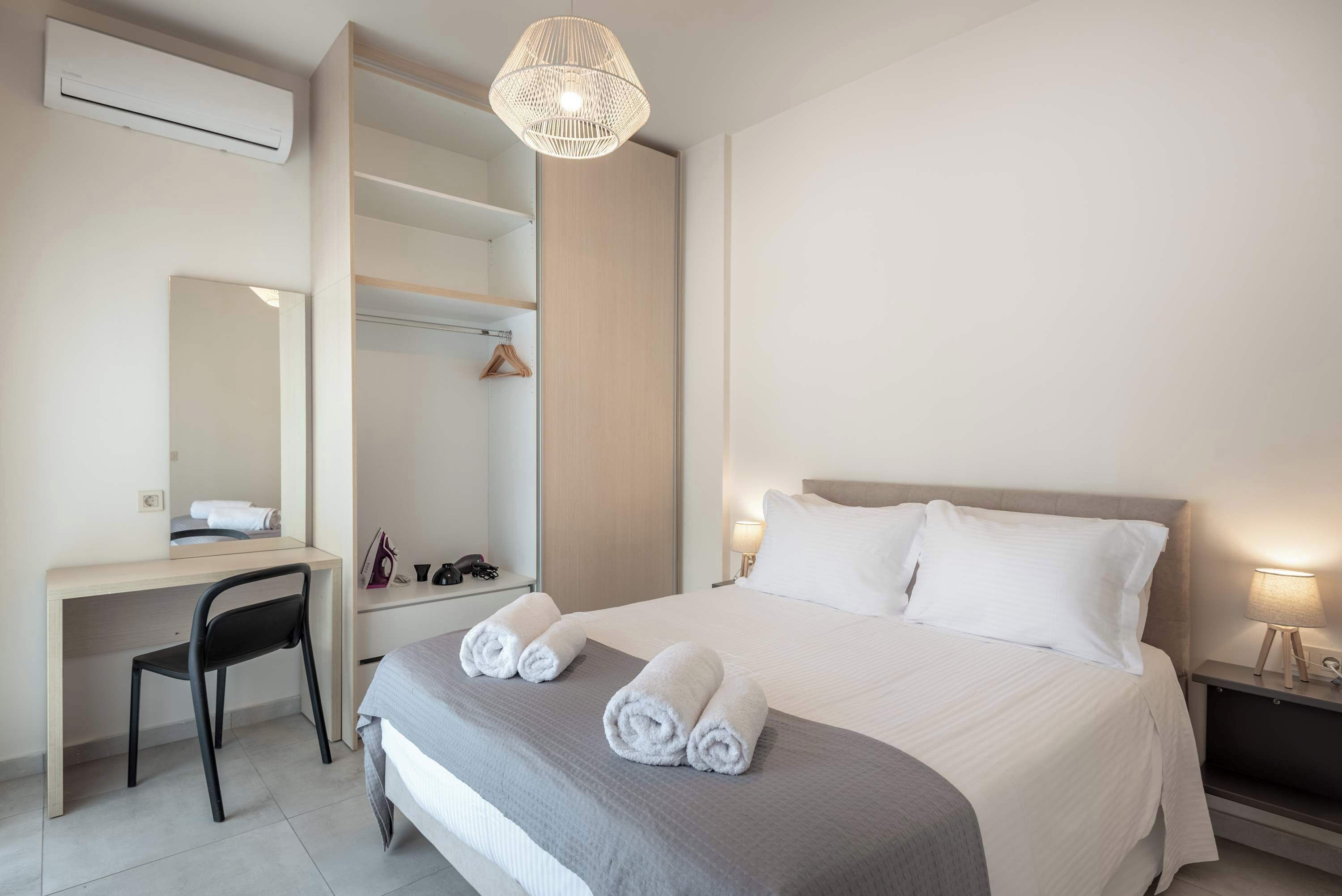 Ein Hotelzimmer mit Bett, Schreibtisch, Stuhl, Kleiderschrank, einer Pendelleuchte und einem Nachttisch mit Lampe.