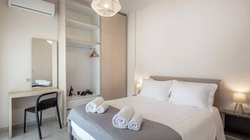 Ein Hotelzimmer mit Bett, Schreibtisch, Stuhl, Kleiderschrank, einer Pendelleuchte und einem Nachttisch mit Lampe.