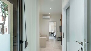 A hallway with a sliding glass door, a beige sofa, a TV mounted on the wall, and an air conditioning unit. - Harma City Living - Street View Family Apartment (Chania)