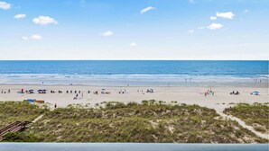 A beach with a clear sky, sandy shore, and a few people and umbrellas. - Beach Club I Unit 5F - Oceanfront! (North Myrtle Beach)