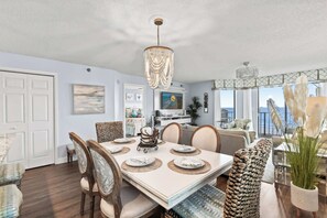 A dining area with a large table, chairs, a chandelier, and a view of the ocean.