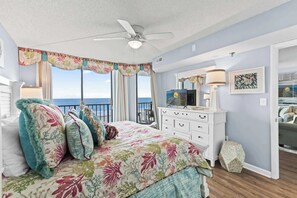 A bedroom with a bed, a ceiling fan, a dresser, a mirror, and a view of the ocean.