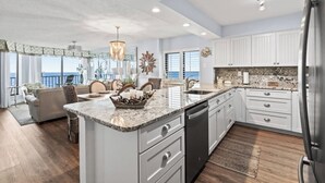 A modern kitchen with white cabinetry, a granite countertop, and a built-in dishwasher. - Beach Club I Unit 5F - Oceanfront! (North Myrtle Beach)