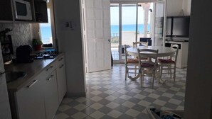 A kitchen with a microwave, stove, and cabinets, leading to a balcony with a view of the sea.