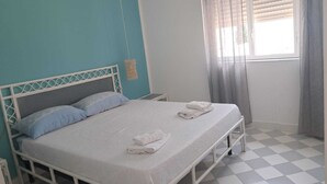 A bedroom with a bed, two pillows, a bedside table, a window with curtains, and a checkered floor. - FIRST TO SCALE (Punta Grande)
