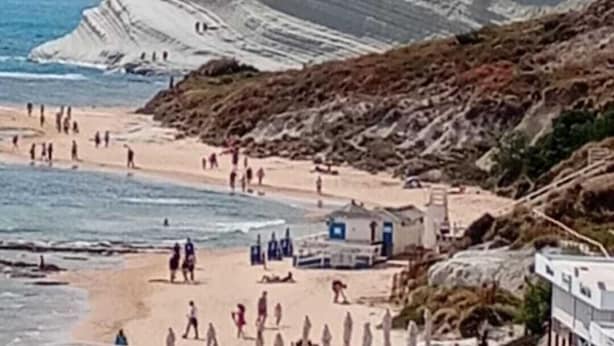 A beach with people, a rocky coastline, and a building with a blue roof. - FIRST TO SCALE (Punta Grande)