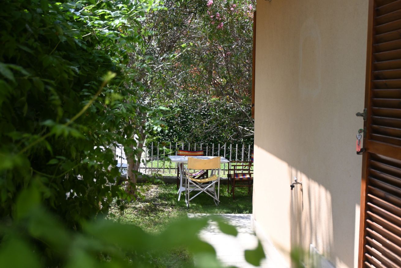 A patio area with a table and chairs, surrounded by greenery and a white fence.