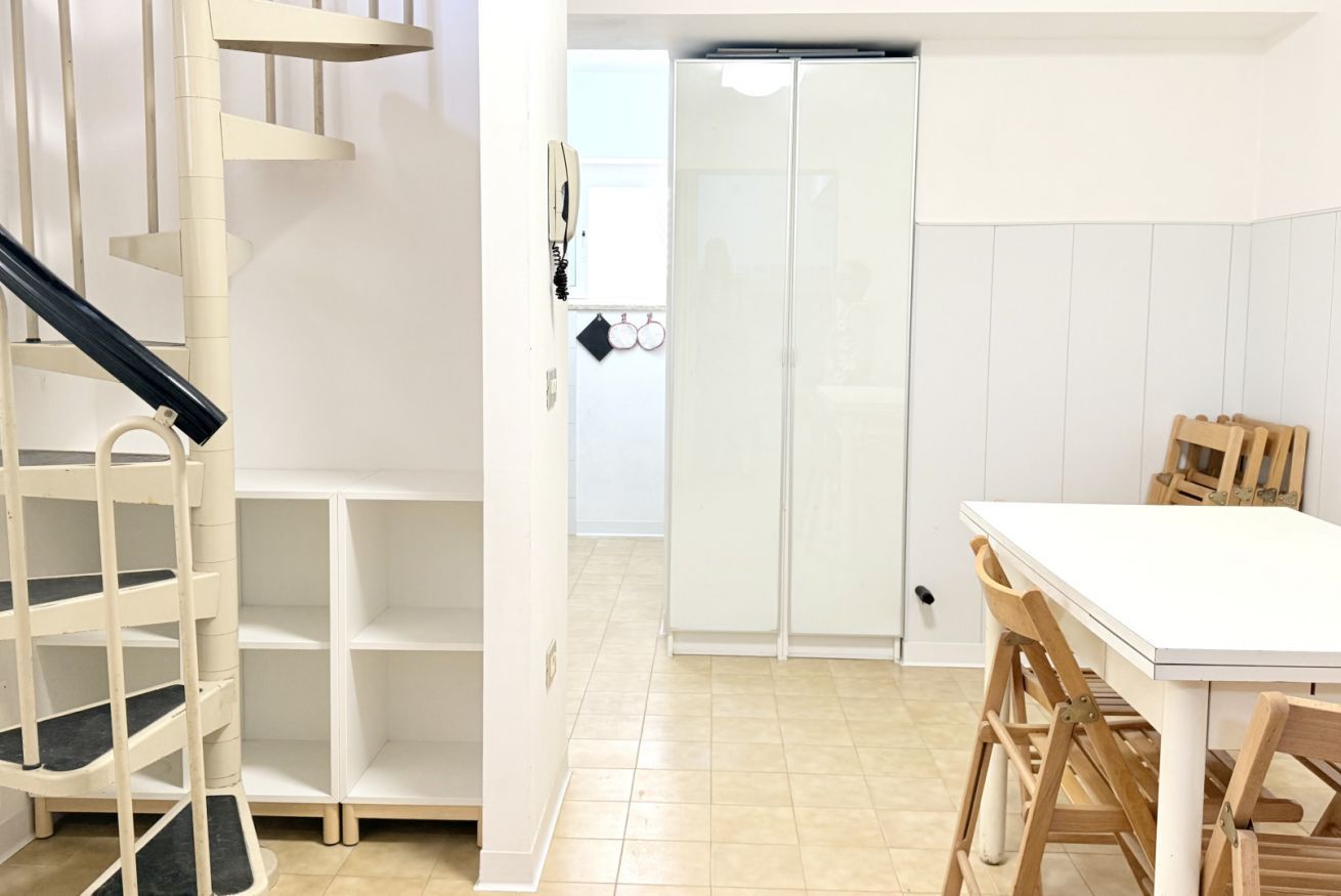 Une pièce dotée d’un escalier en colimaçon, d’une armoire blanche, d’une table à manger avec des chaises et d’un sol carrelé.
