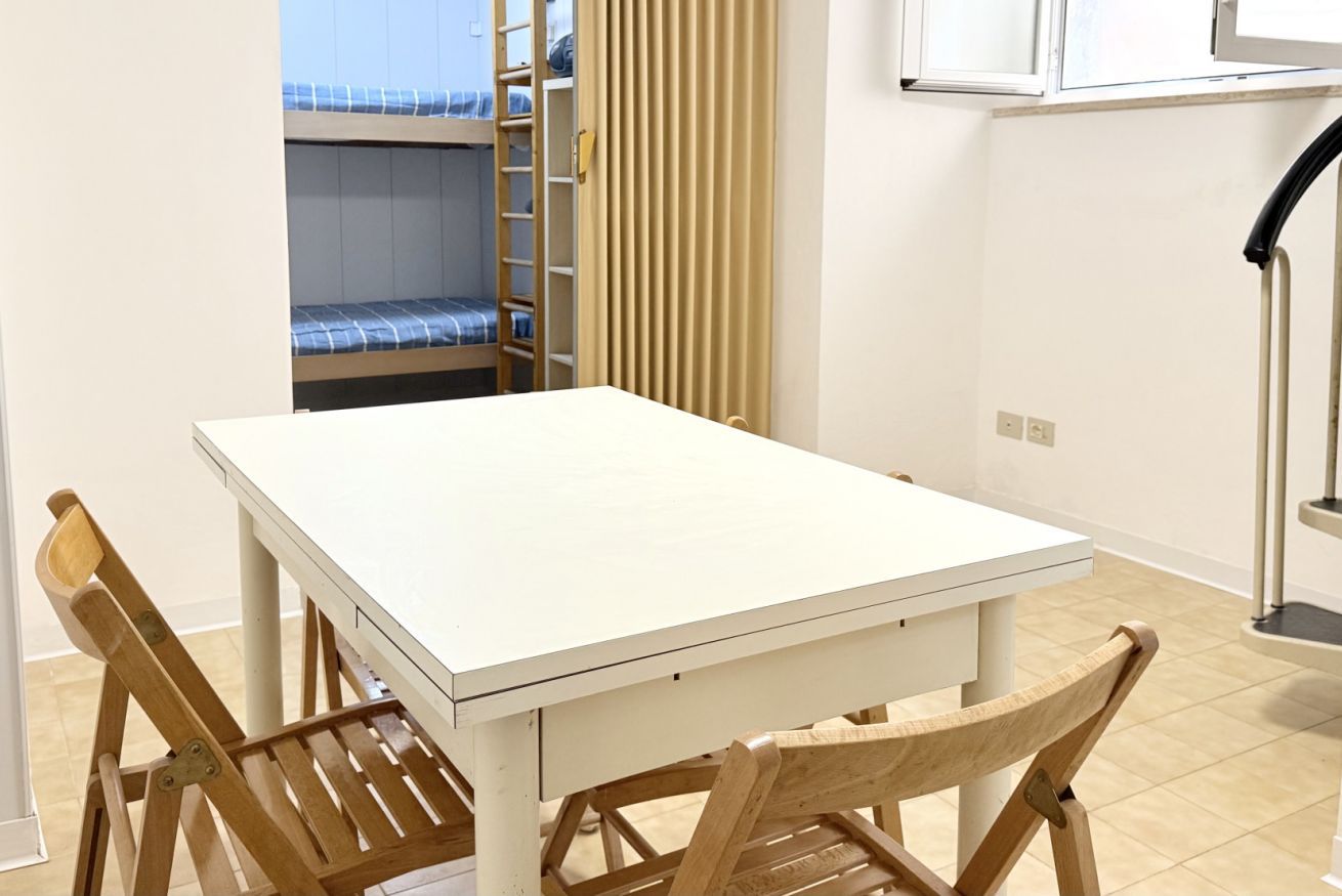 A room with a white table, wooden chairs, a bunk bed, a sliding door, and a cabinet.