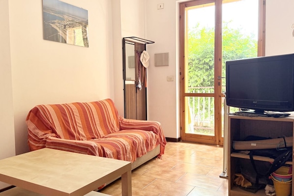 A living room with a sofa, a table, a television, and a sliding glass door leading to an outdoor area.