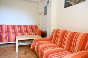 A living room with a striped sofa, a small wooden table, and a white wall with a clock and a framed picture.
