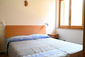 A bedroom with a wooden headboard, a bed with striped bedding, a nightstand, and a window with a wooden frame.