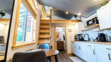 A compact kitchen with a dining area, wooden ceiling, and a view through a window.