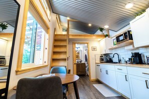 A compact kitchen with a dining area, wooden ceiling, and a view through a window. - Orange Poppy - Seward Alaska Modern Forest Tiny Home Retreat Near Kenai Fjords (Seward)