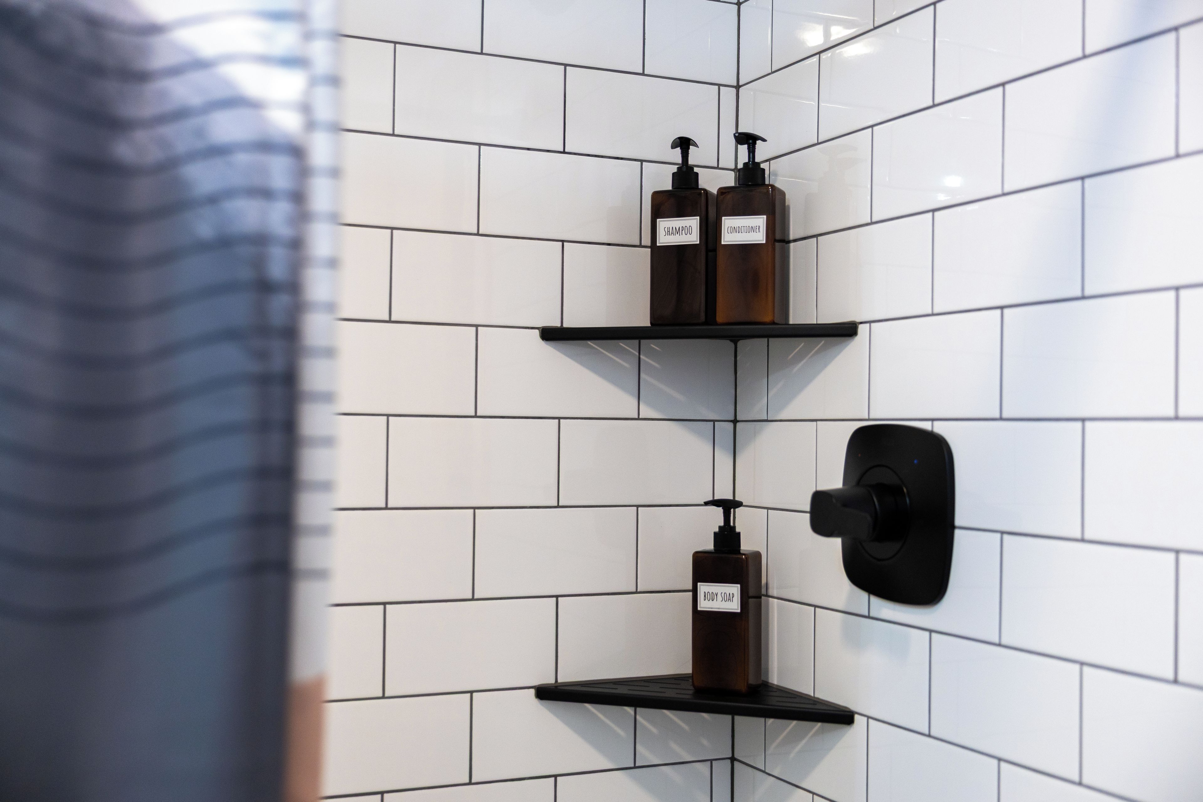 Une salle de bain avec des murs recouverts de carreaux blancs et trois étagères où sont rangés les articles de toilette.