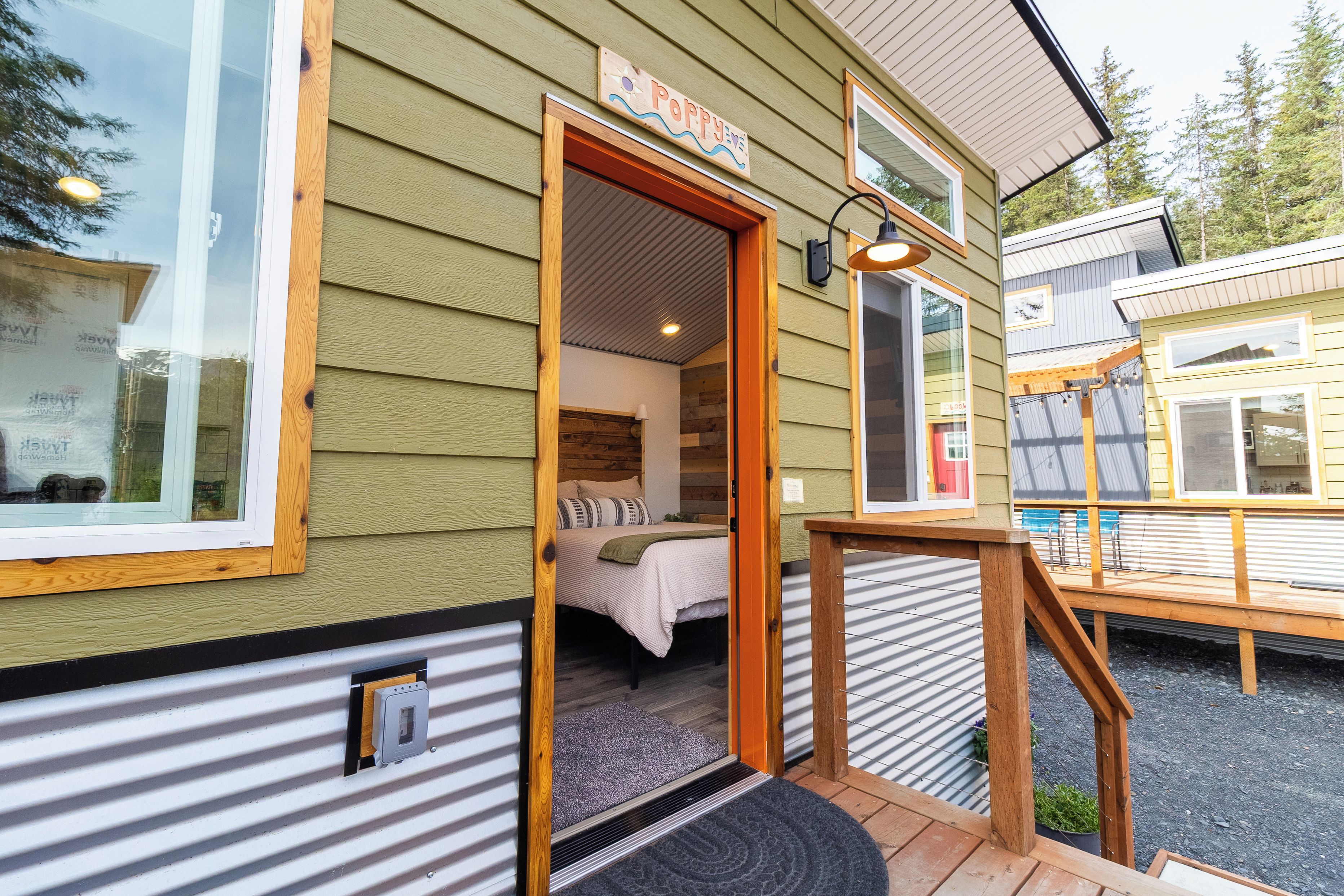A wooden cabin with a visible bedroom, a porch with a bench, and a sign that reads 'Poppy'.