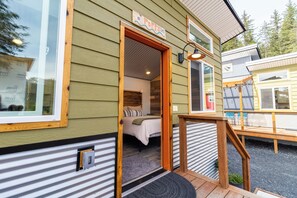 A wooden cabin with a visible bedroom, a porch with a bench, and a sign that reads 'Poppy'. - Orange Poppy - Seward Alaska Modern Forest Tiny Home Retreat Near Kenai Fjords (Seward)