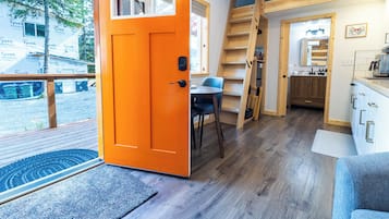 A compact, modern interior with a bright orange door, a small dining area, and a kitchen with wooden accents.