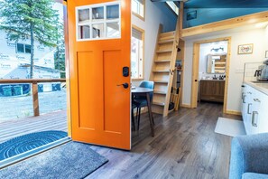A compact, modern interior with a bright orange door, a small dining area, and a kitchen with wooden accents. - Orange Poppy - Seward Alaska Modern Forest Tiny Home Retreat Near Kenai Fjords (Seward)