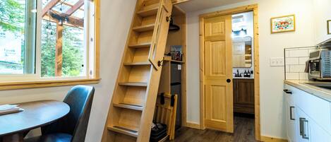 A compact kitchen with wooden cabinets, a dining area with a table and chairs, and a wooden staircase leading to a loft.