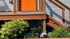 A house with a green exterior, a wooden deck, a red door, and a window with a wooden frame. - Orange Poppy - Seward Alaska Modern Forest Tiny Home Retreat Near Kenai Fjords (Seward)