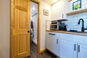 A compact kitchen with white cabinets, a microwave, and a sink. - Orange Poppy - Seward Alaska Modern Forest Tiny Home Retreat Near Kenai Fjords (Seward)