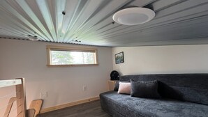 A room with a grey sofa, a window, a wooden chair, and a ceiling with a ribbed design. - Orange Poppy - Seward Alaska Modern Forest Tiny Home Retreat Near Kenai Fjords (Seward)