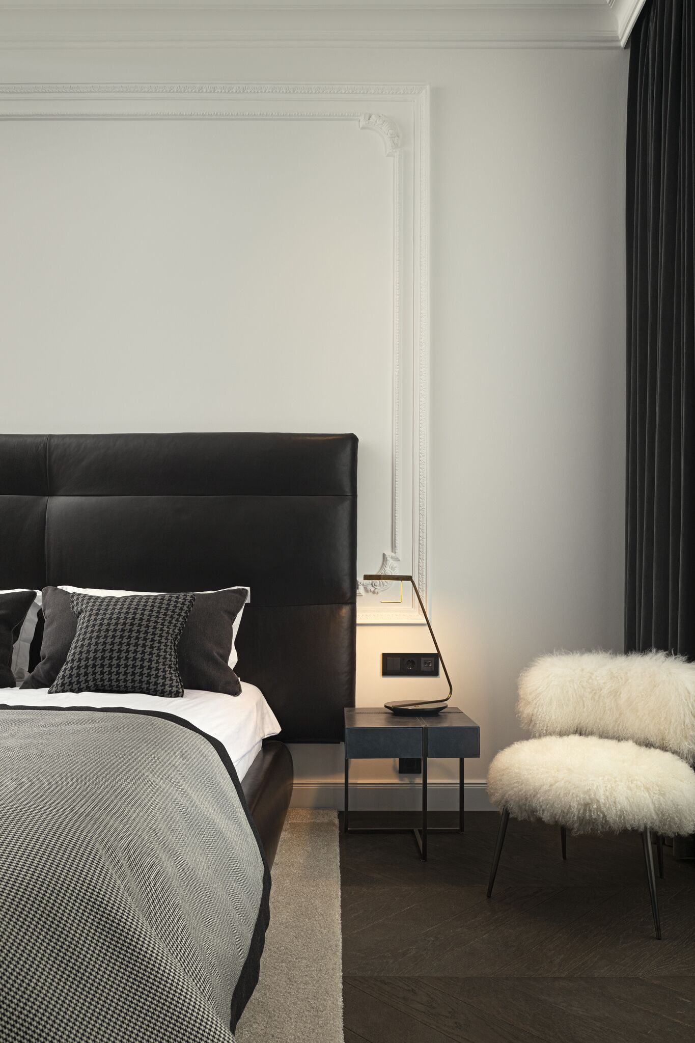 A modern bedroom with a large bed, a bedside table with a lamp, and a fluffy chair.